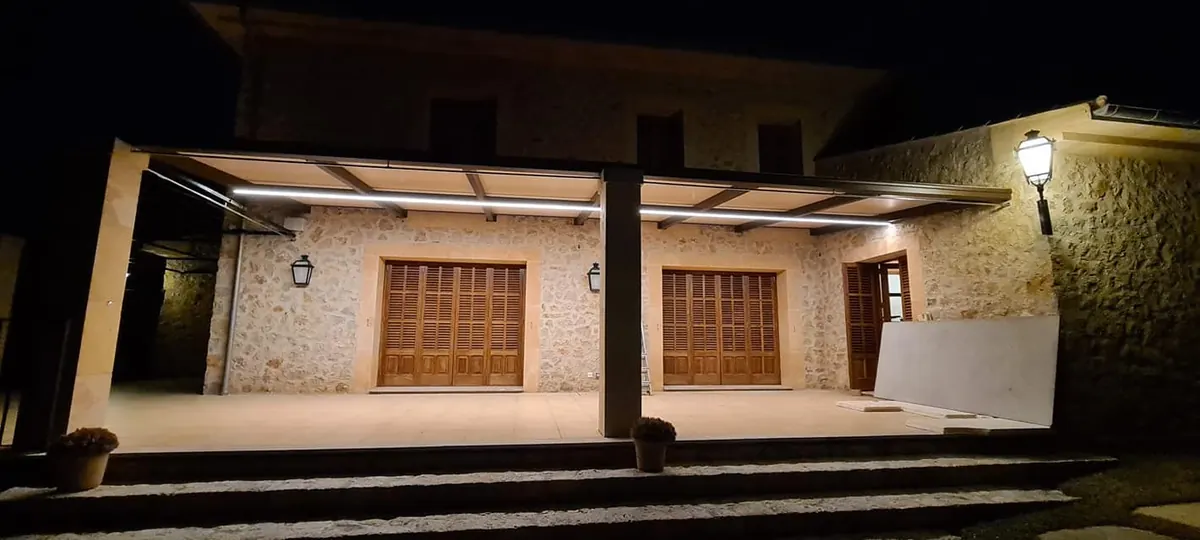 Pérgola con toldo corredero e iluminación LED en una casa de piedra de noche