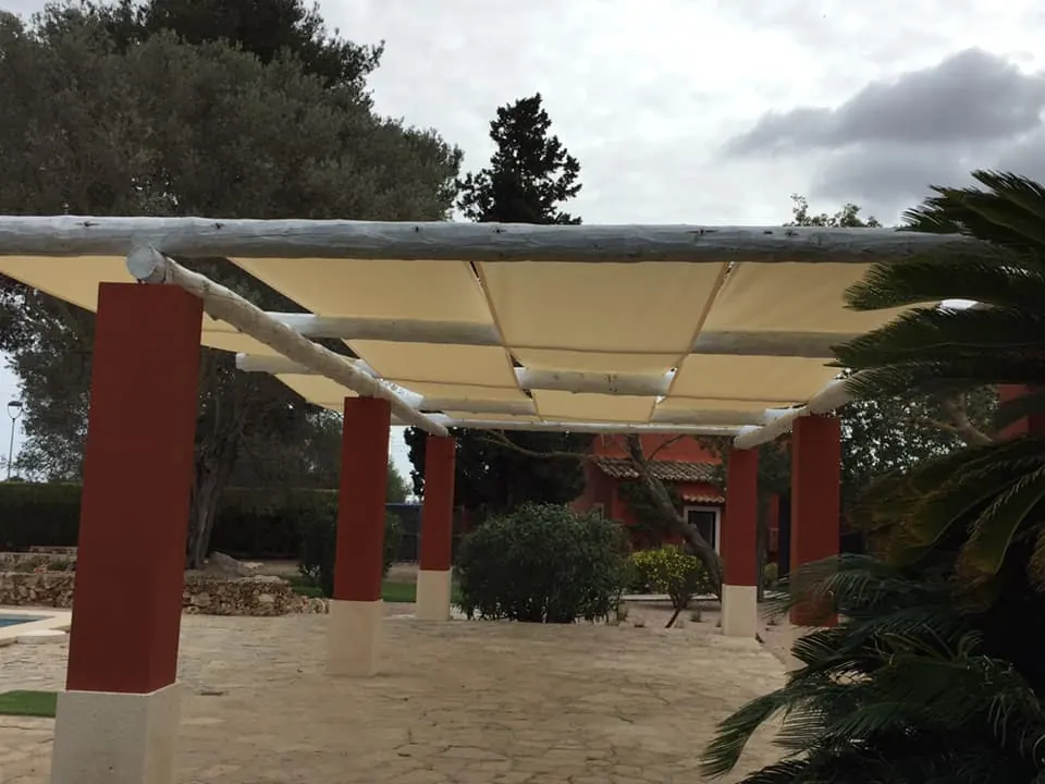 Pérgola rústica de madera con lonas tensadas color crema en un jardín