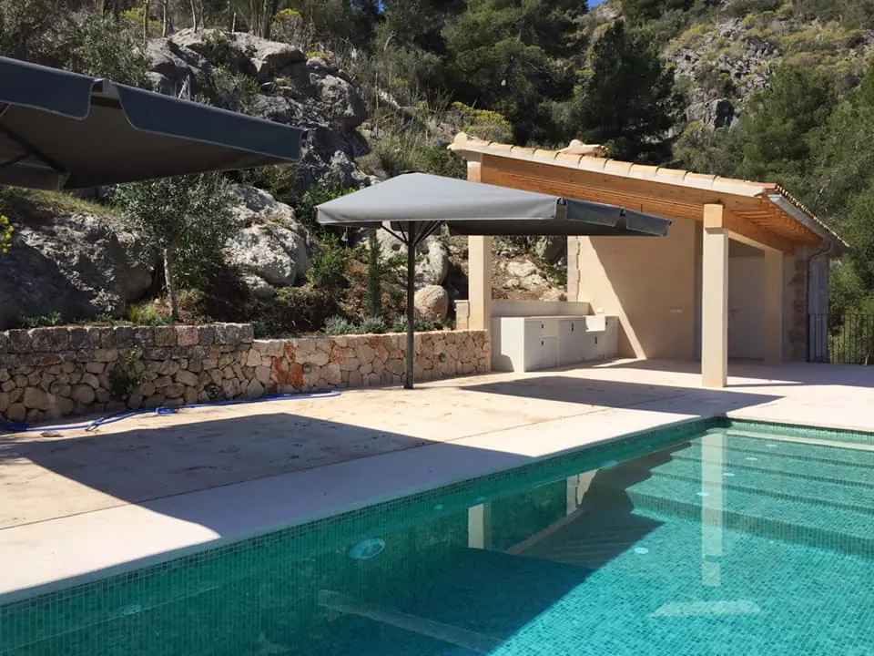 Sombrilla gris cuadrada dando sombra a la zona de piscina de una villa