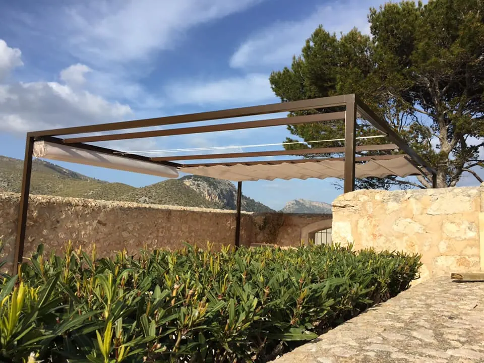 Pérgola metálica con toldo corredero sobre terraza con pared de piedra en Mallorca